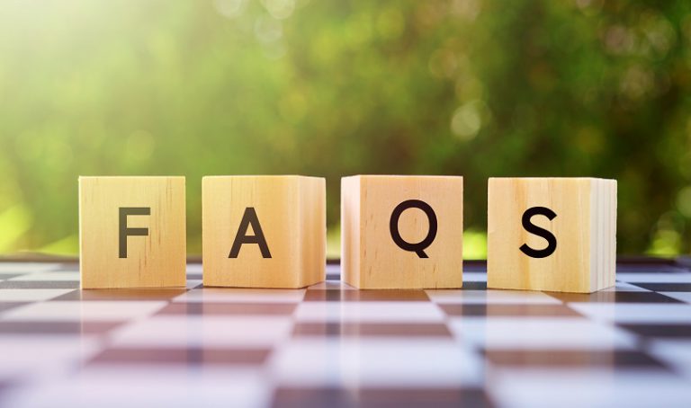 Des blocs de bois orthographiant « FAQ » sont disposés sur une surface à carreaux, avec un fond extérieur vert à mise au point douce, éclairé par la lumière naturelle du soleil.