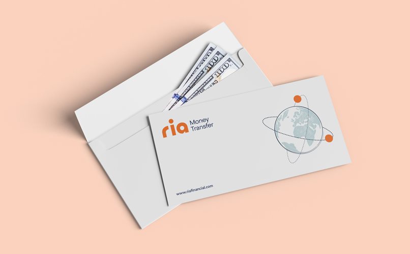 An envelope with the "ria Money Transfer" logo is partially open, revealing several U.S. hundred-dollar bills inside. The envelope has a globe graphic with orbiting dots. The background is a light peach color.